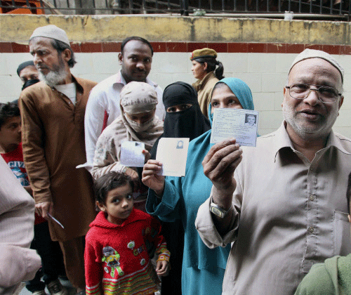 People stand in queues to cast their votes for Delhi Assembly elections, at a polling station in New Delhi. PTI Photo