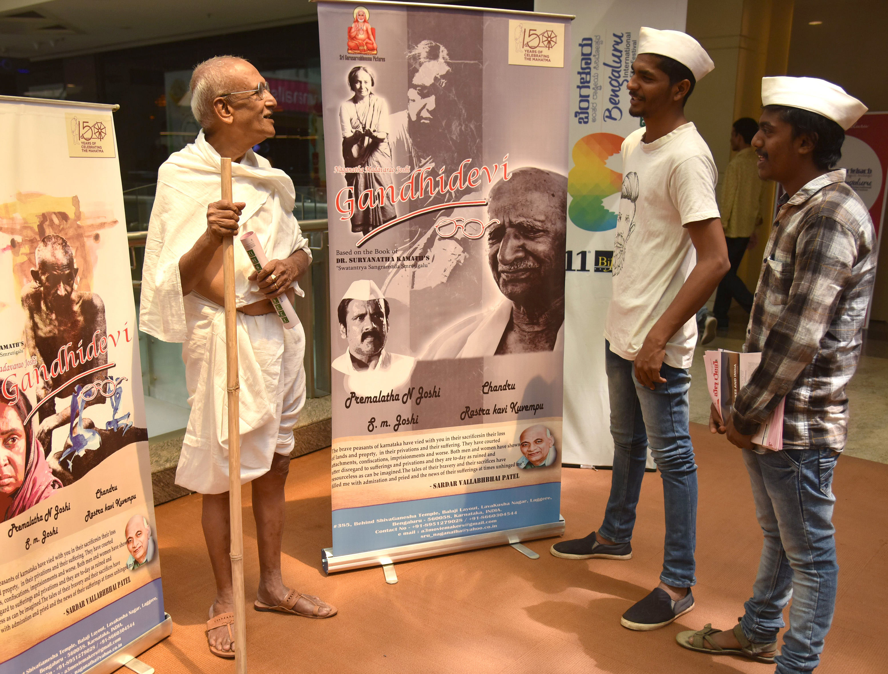 Vemgal Somashekar dressed like Mahatma Gandhi stands next to Gandhidevi film poster at BIFFes 2019. DH Photo by SK Dinesh