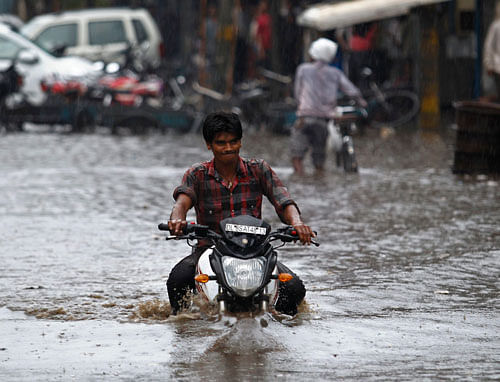 A man rides a motorcycle through a flooded street after a heavy monsoon rain shower in New Delhi July 20, 2013. India's monsoon rains turned average last week and may pick up over areas that grow cane, oilseed and cotton in northern and western regions next week, weather department officials said, helping most summer crops into their last leg of planting. REUTERS