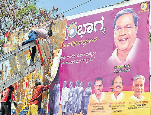 Mysore City Corporation employees remove posters of the State government, following the announcement of model code of conduct, in Mysore, on Wednesday. DH Photo