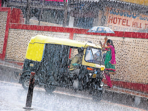 A passenger makes an effort to board an auto amidst rain in Madikeri. DH Photo