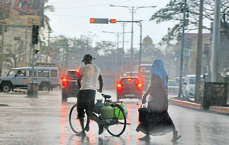 A man carries water pots on his bicycle even as it rains in Gadag on Thursday. DH Photo