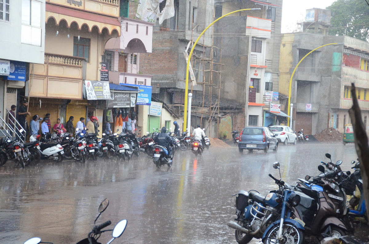 People taking shelter before shops during the downpour at Patil Galli in Belagavi on Tuesday.