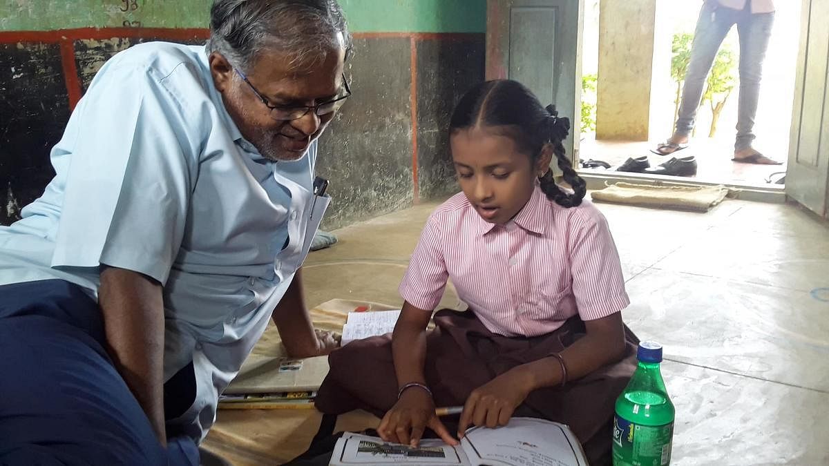 MLA Suresh Kumar listens to Nanditha as she reads out a poem for him at the Obenahalli government school, Srinivaspur taluk in Kolar district.