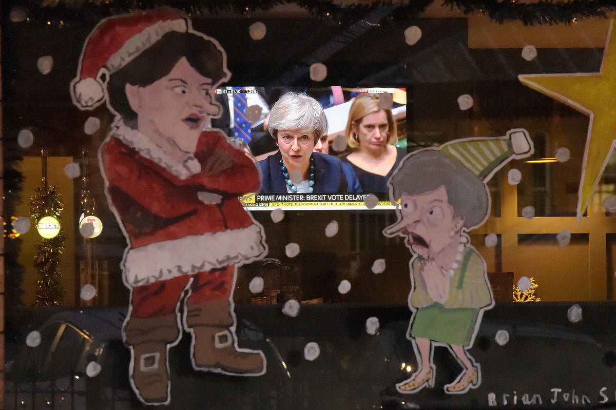 People in a bar watch Britain's Prime Minister Theresa May during a debate in the house of Commons on television as a window is illustrated with DUP leader Arlene Foster as Santa Claus and Theresa May as a Christmas Elf in Lisburn, Northern Ireland Decemb