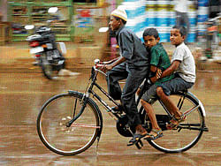 pitter-patter: Children ride a bicycle in the rain in Chikkaballapur City. DH photo