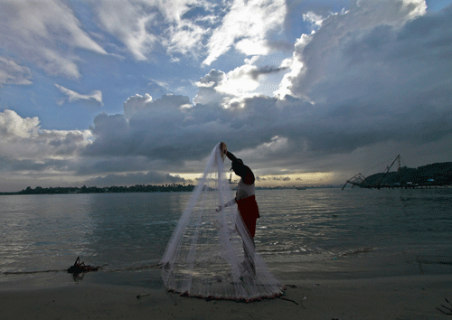 A fisherman arranges his fishing net at a beach against the backdrop of pre-monsoon clouds in Kochi June 5, 2014. Reuters
