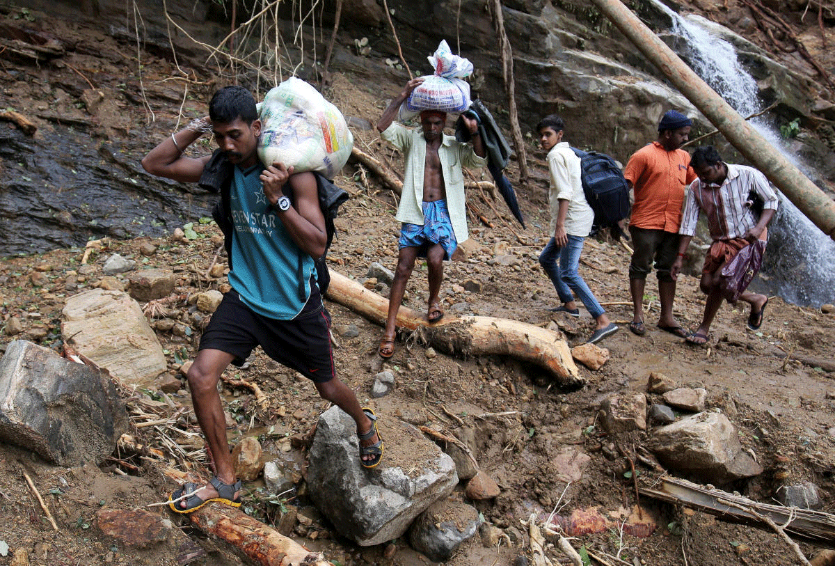 Flood victims carry relief material as they walk through a damaged area after floods, at Nelliyampathy Village, Kerala. Reuters Photo