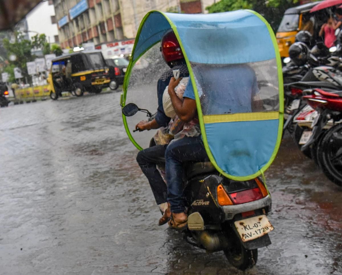 People ride a scooter with a cover as it rains in Kochi. The southwest monsoon arrived in Kerala on Tuesday, three days ahead of schedule. PTI