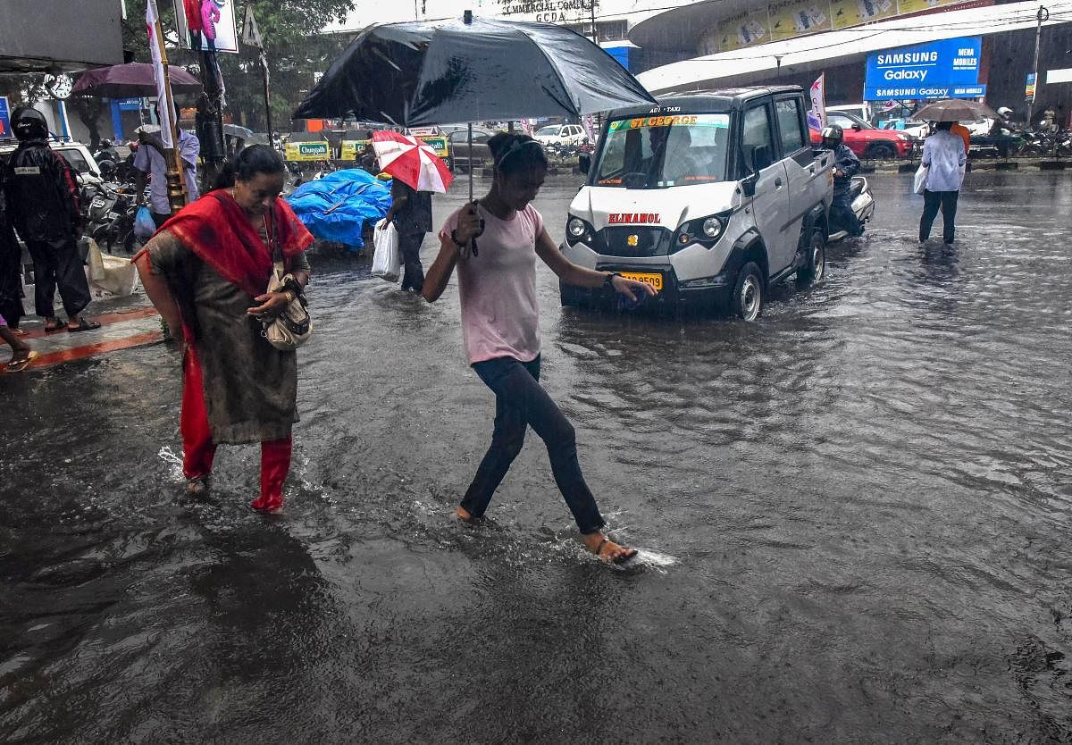 Pedestrians hold umbrellas while trying to make their way across a street in pouring rain, in Kochi on Monday. PTI