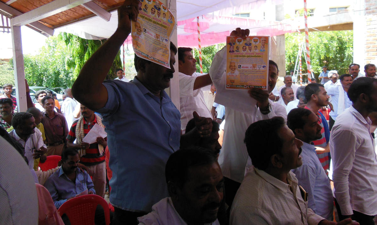 A group of people display BJP pamphlets at a Congress meeting at Channarayapatna, Hassan district on Thursday.