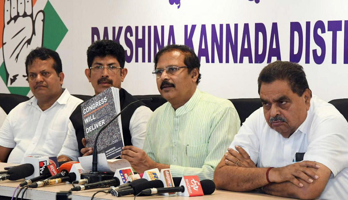 KPCC Vice President V R Sudarshan releases the Congress manifesto 'We will deliver' at the district Congress committee office in Mangaluru on Friday. Former minister B Ramanath Rai and District Congress Committee spokesperson A C Vinayraj look on.
