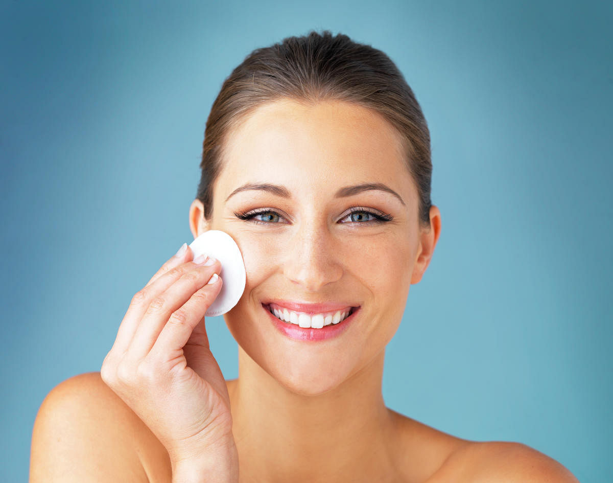 Studio portrait of a beautiful young woman wiping her face with a cotton pad against a blue backgroundStudio portrait of a beautiful young woman wiping her face with a cotton pad against a blue background