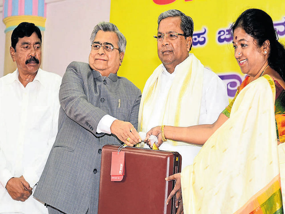 Assembly Speaker K&#8200;B&#8200;Koliwad gives a briefcase to Mohana Kumari, the newly elected MLA&#8200;from Gundlupet, after  she took oath in Bengaluru on Friday. Kalale Keshavamurthy (left), the newly elected MLA&#8200;from Nanjangud, and Chief  Minister Siddaramaiah are seen. DH&#8200;Photo