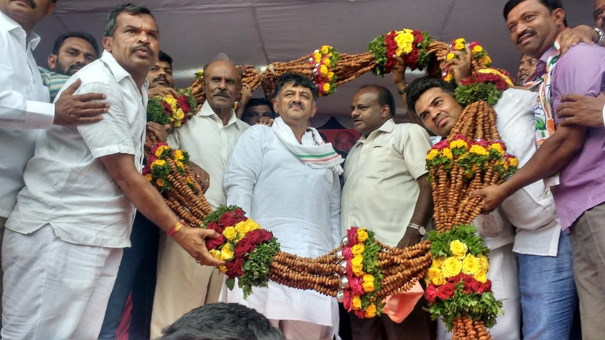 Supporters faciliate Water Resources Minister D K Shivakumar and Chief Minister H D Kumararaswamy with a garland of almonds during an election meeting in Kunigal, Tumakuru district on Friday. DH Photo