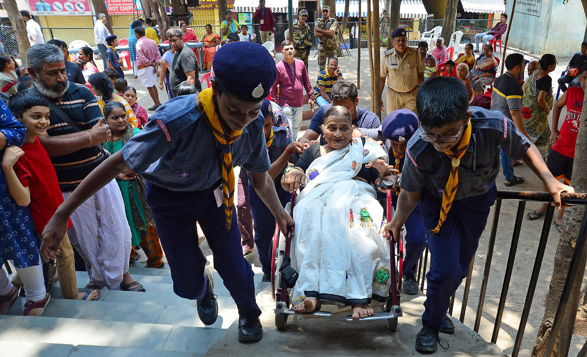 Scoutsh help carry a wheelchair-bound woman to her polling station.