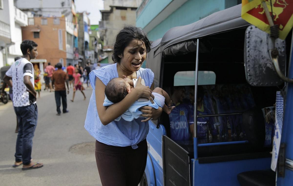 A Sri Lankan woman runs for safety with her infant after police found explosive devices in a parked vehicle in Colombo on Monday. AP/PTI