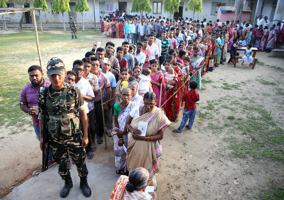 A Sashastra Seema Bal (SSB) trooper stands guard as people wait in queues to cast their votes outside a polling station in Khowai, Tripura. REUTERS