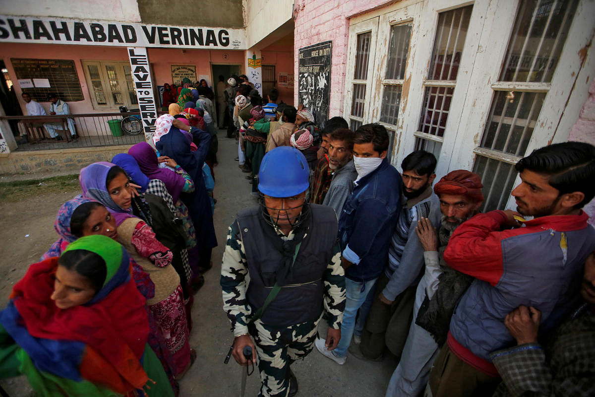 An Indian policeman stands guard as people wait in queues to cast their votes outside a polling station during the third phase of general election in Verinag in south Kashmir's Anantnag district April 23, 2019. (REUTERS)