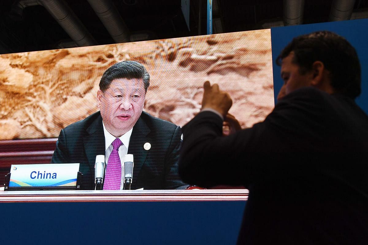 A journalist takes photos as a screen behind him shows a live image of Chinese President Xi Jinping speaking at the leaders summit of the Belt and Road Forum, in the media center of the Forum in Beijing on April 27, 2019. (AFP)
