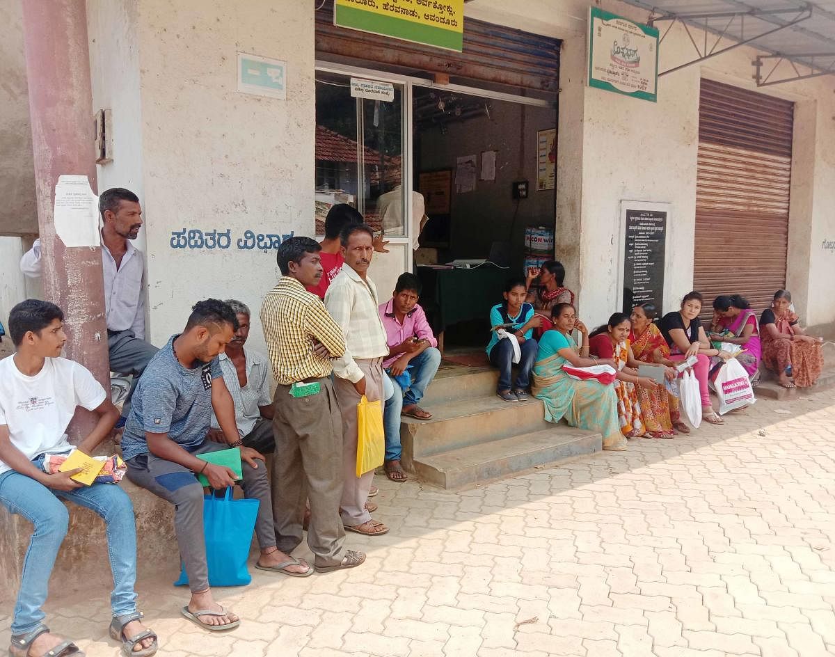 People wait outside the fair price shop near the Gram Panchayat office in Bettageri.