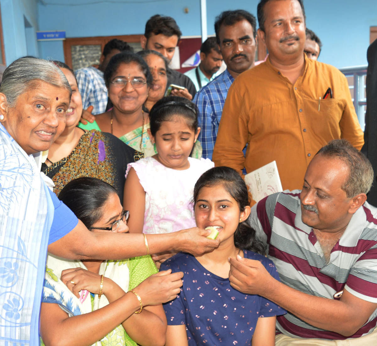 Family members and friends feed sweet to Srujana D, a student of St Philomena English High School, Attibele, who has scored 625/625 in SSLC examination, in Anekal on Tuesday.