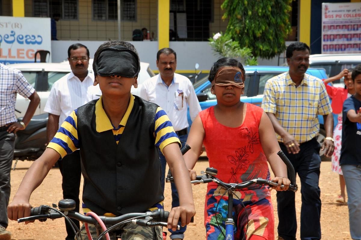 Students ride bicycles blindfolded in Chikkamagaluru on Thursday. DH photo