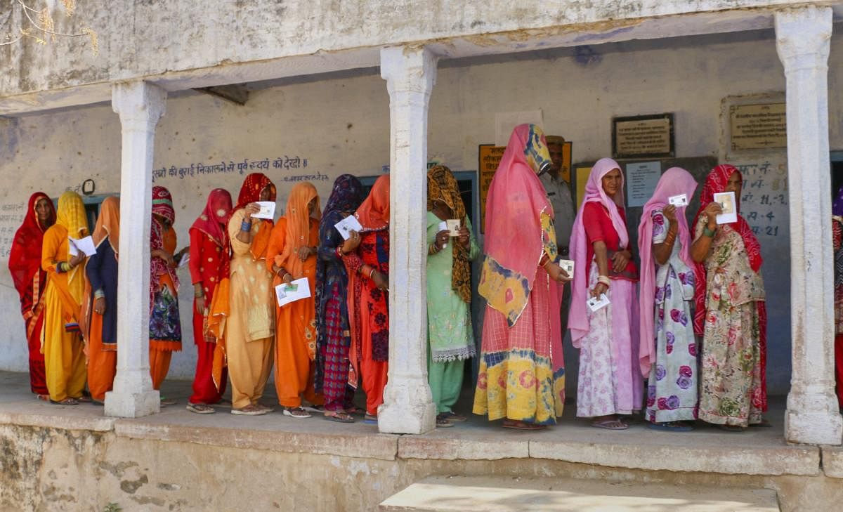 Voters show their ID cards as they wait in a queue at a polling station, during the fifth phase of Lok Sabha elections, in Nagaur district. PTI photo
