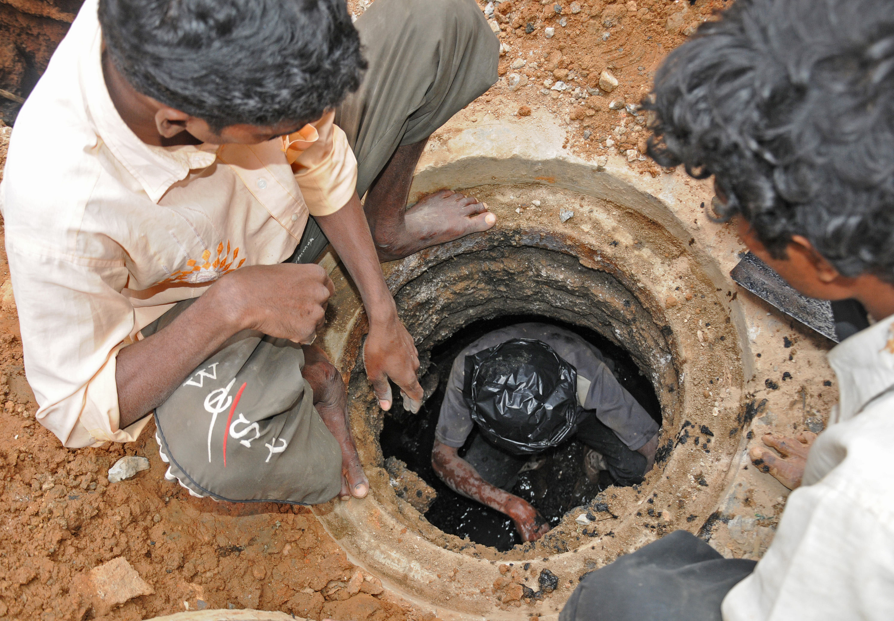 Workers clean a manhole without gloves and shoes at Siddegowda Street, near KH (Double) Road, Bengaluru. This picture was taken in 2013, after the High Court had instructed BWSSB to procure cleaning machines to prevent accidents. DH PHOTO BY S K DINESH