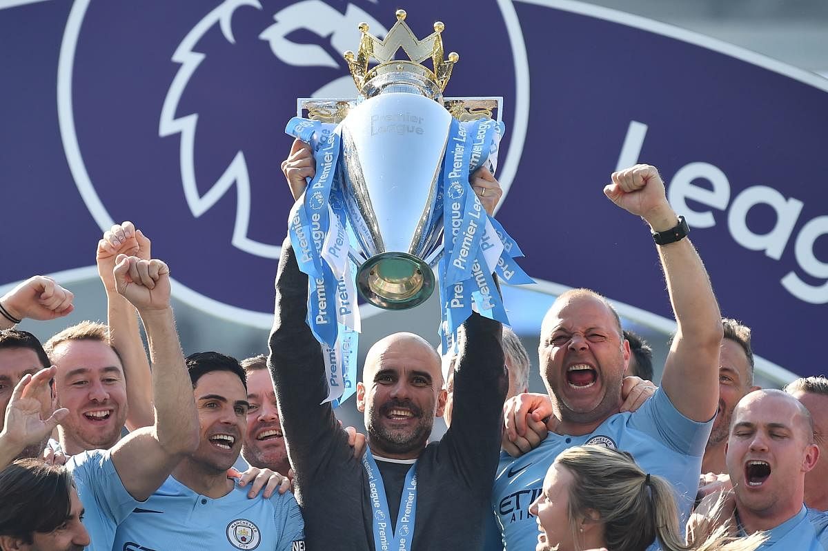 TOPSHOT - Manchester City's Spanish manager Pep Guardiola holds up the Premier League trophy as he's surrounded by his staff after their 4-1 victory in the English Premier League football match between Brighton and Hove Albion and Manchester City at the A