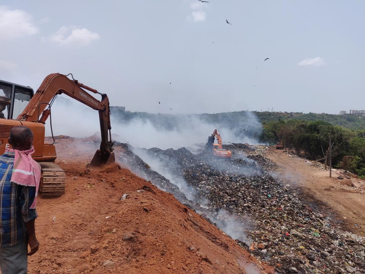Earthmovers being used to throw soil on the fire at the Pacchanady dump yard in Mangaluru on Monday.