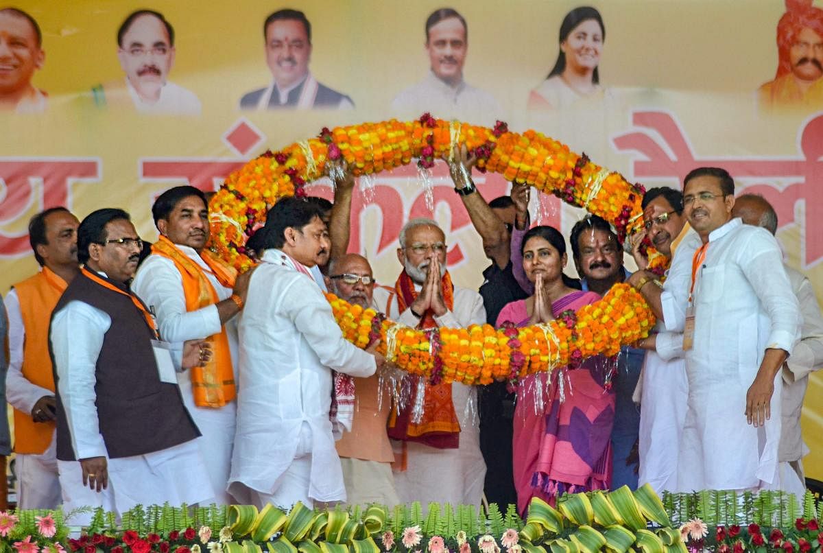 Prime Minister Narendra Modi with NDA candidate for Mirzapur parliamentary seat Anupriya Patel (R) being garlanded during an election campaign rally for the ongoing Lok Sabha polls, in Mirzapur, Thursday, May 16, 2019. (PTI Photo)