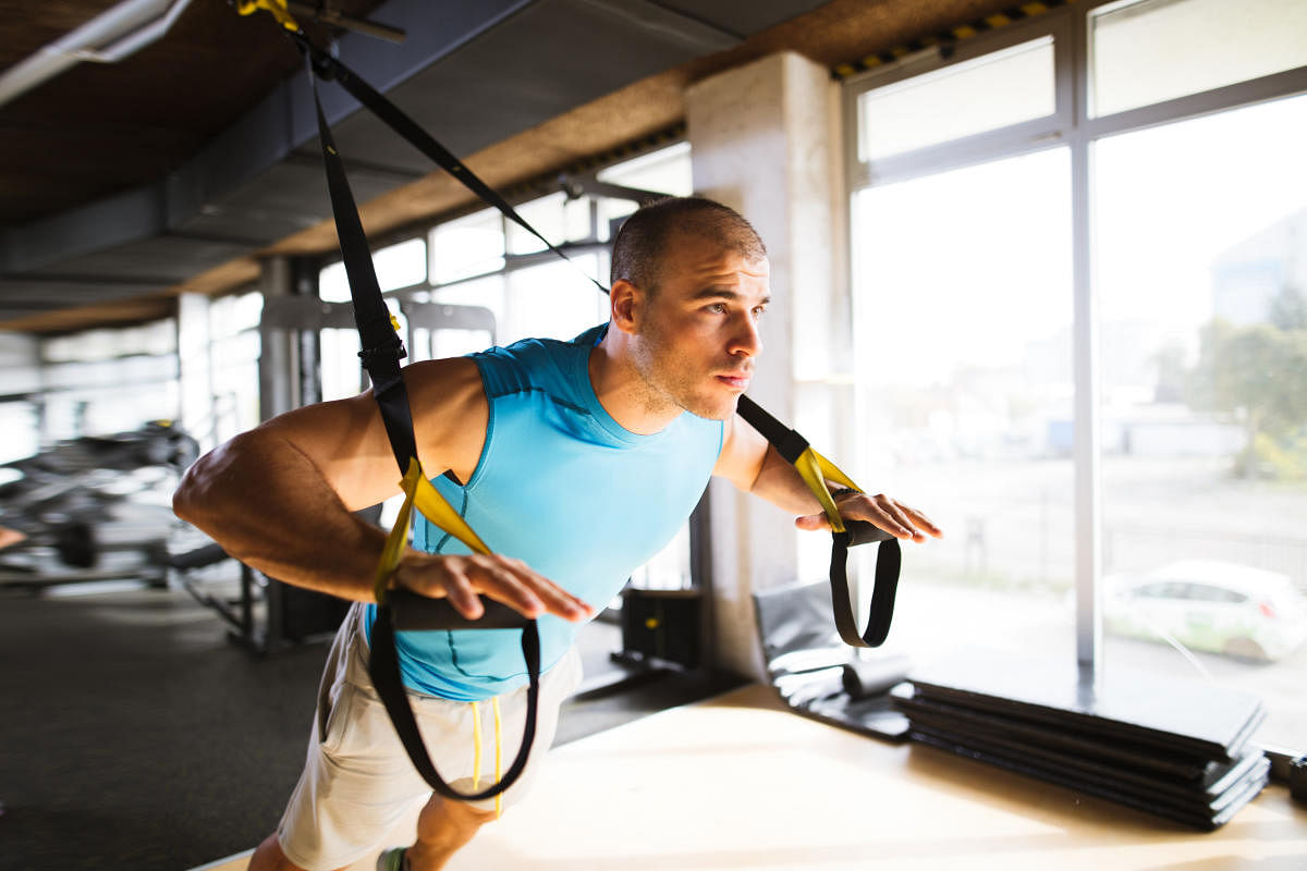 Young athletic man having sports training and doing arm exercises with suspension straps at gym. File photo