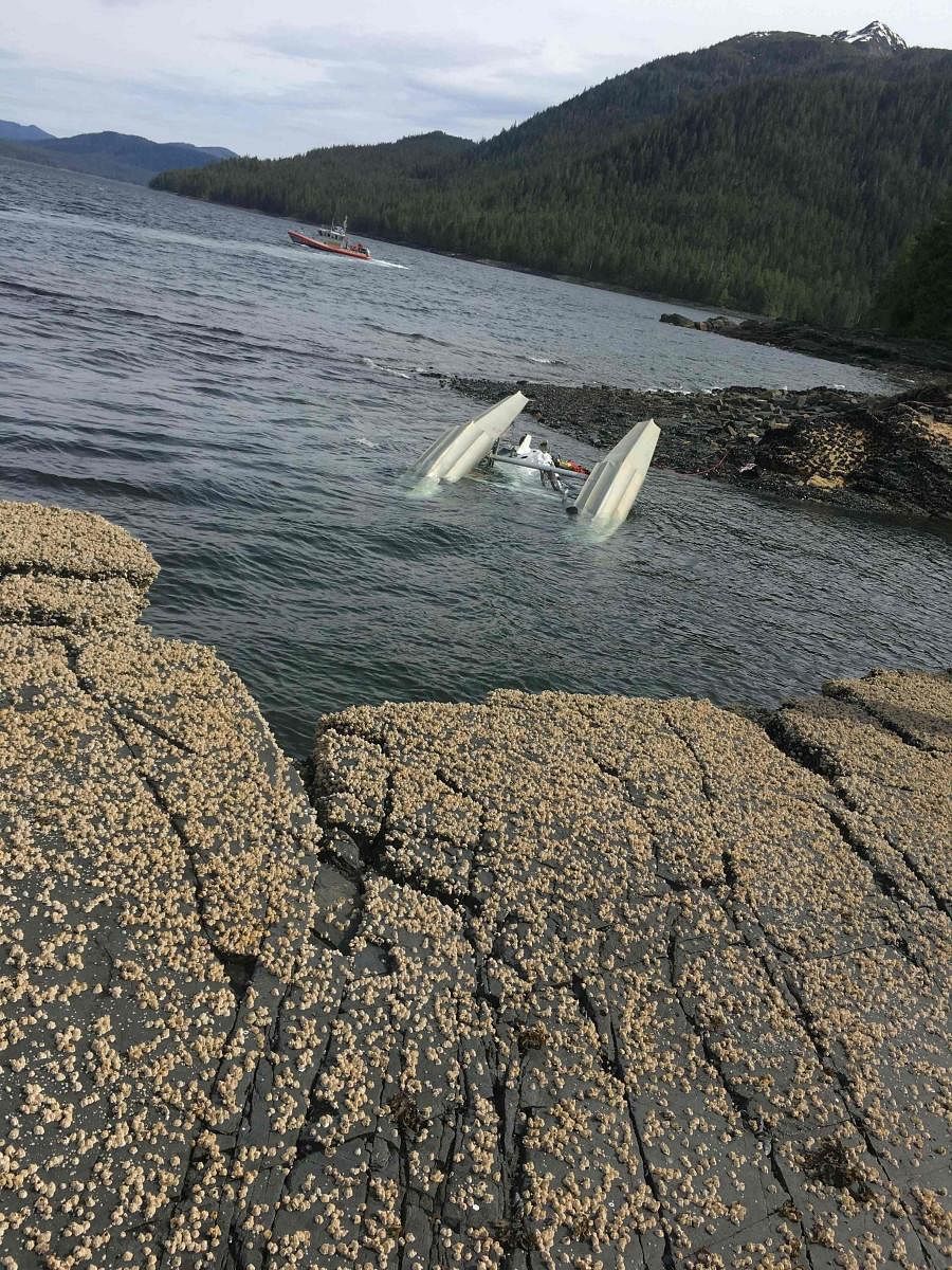 In this image courtesy of Ryan Sinkey and released by the US Coast Guard (USCG), a floatplane lies upside down after a mid-air collision with another plane on May 13, 2019, in Ketchikan, Alaska, as a USCG crew (rear) searches for survivors. (Photo by Ryan