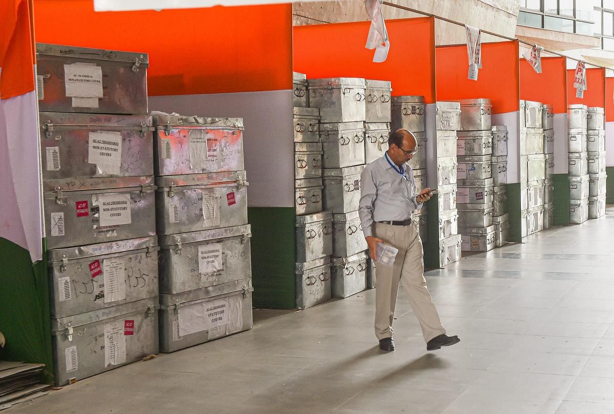An officals looks at his phone as he walks past the boxes containing election material at a counting hall, ahead of the counting process for the 2019 Lok Sabha elections, at Akshardham in New Delhi, Wednesday, May 22, 2019. (PTI Photo)