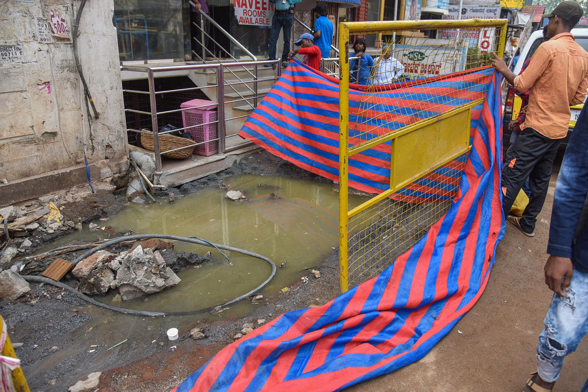 Workers cover a sewage pit on Cottonpet Main Road before the arrival of the mayor on Monday. DH photo/S K Dinesh