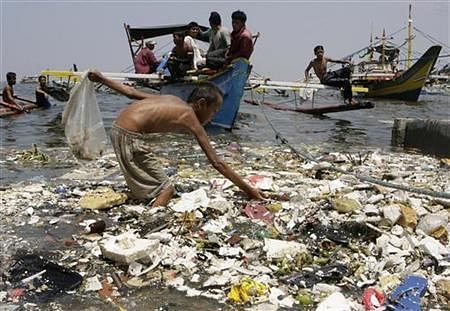 A boy collects plastic materials as boats dock near a polluted coastline in Manila April 9, 2008. Credit: Reuters/Cheryl Ravelo