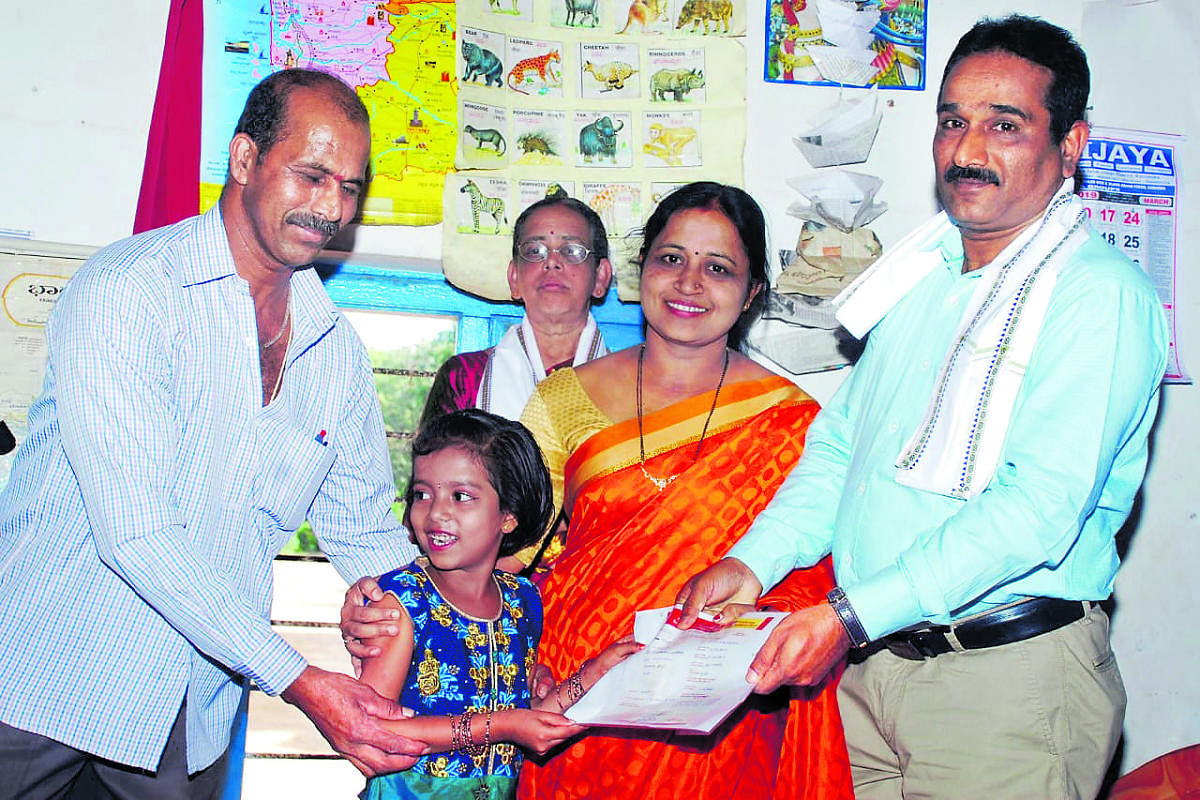 Ravindra Hegde, headmaster of Government School at Mudradi Nellikatte, hands over deposit certificate to a child of Class I of Government School at Bannampalli near Padigara, Hebri.