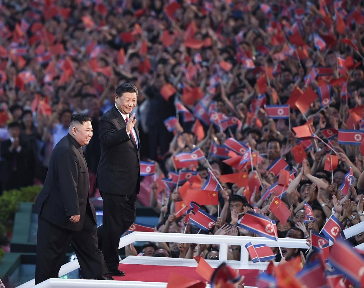 In this Thursday, June 20, 2019, file photo released by China's Xinhua News Agency, spectators wave Chinese and North Korean flags as North Korean leader Kim Jong Un, left, and visiting Chinese President Xi Jinping attend a mass gymnastic performance at t