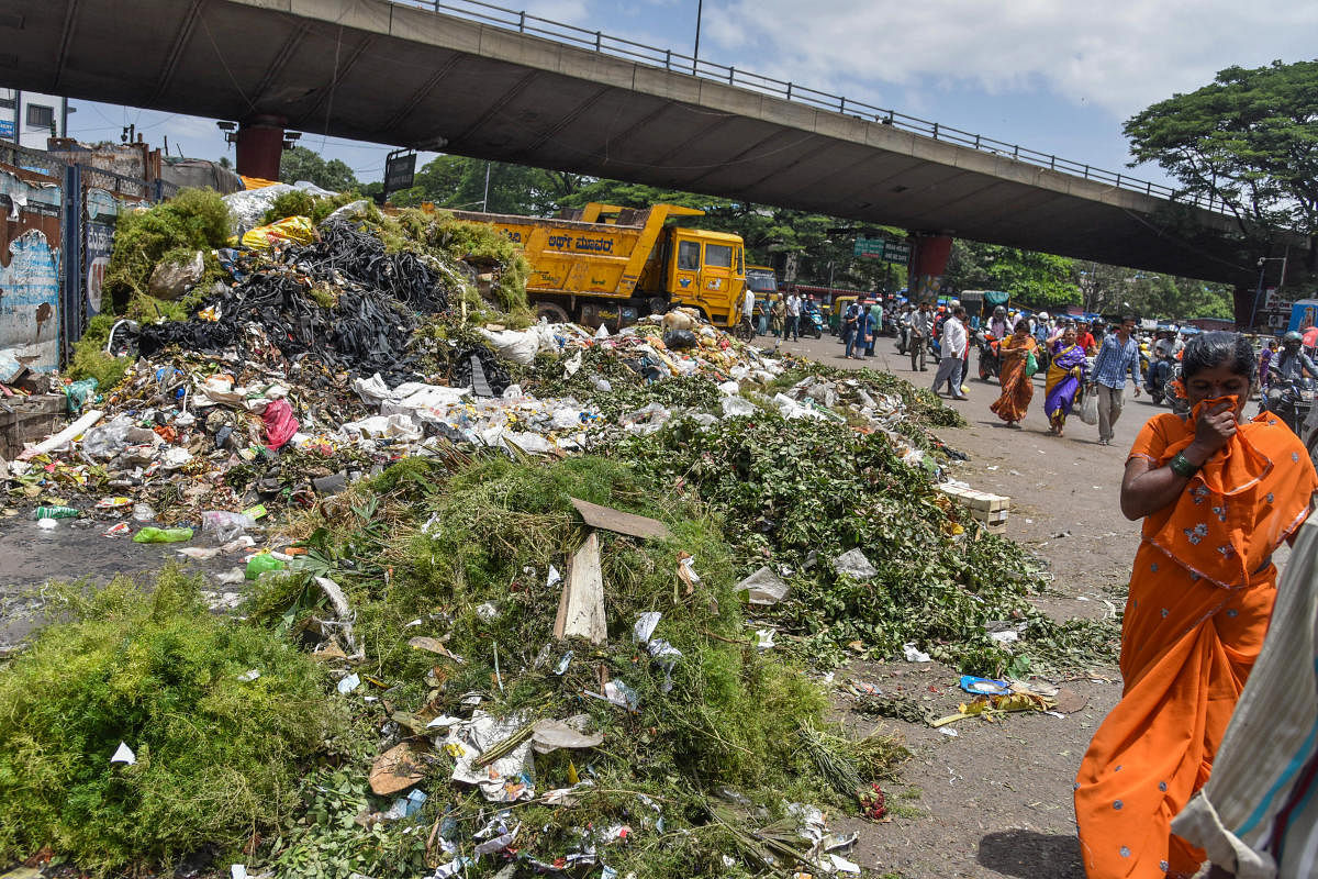 A woman covers her nose as she passes by the garbage mound at KR Market in Bengaluru on Friday. DH PHOTO/S K DINESH