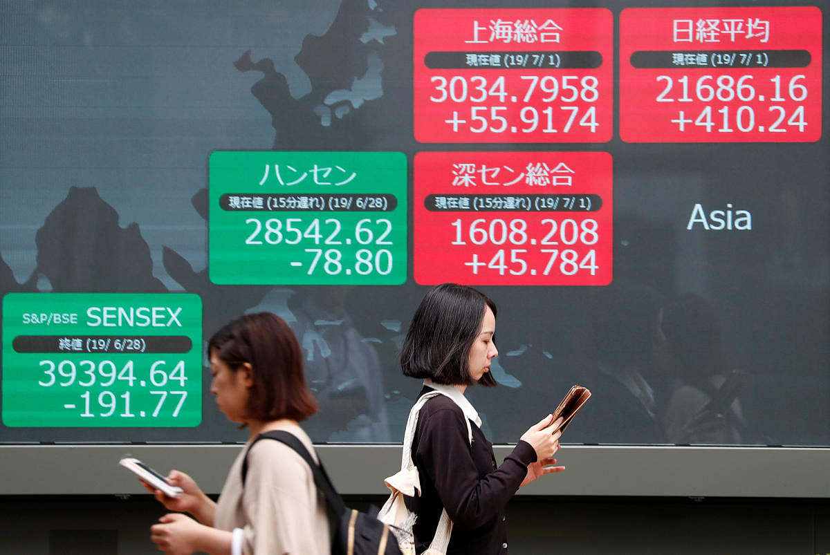 Passersby walk past an electric screen showing Asian markets indices outside a brokerage in Tokyo. (Reuters Photo)