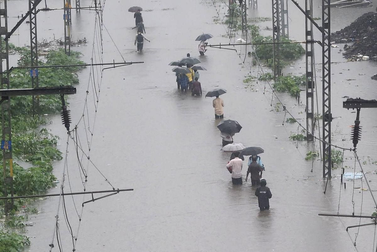People walk on the waterlogged railway tracks during heavy monsoon rain at Tilak Nagar station in Mumbai on Tuesday. PTI photo