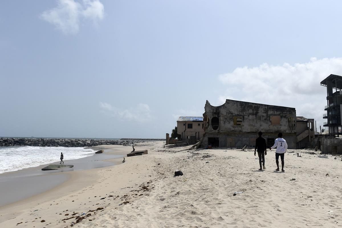 People walk along the beach toward houses destroyed by tidal erosion at Alpha Beach, a strip of the Lagos Coastline. (AFP Photo)