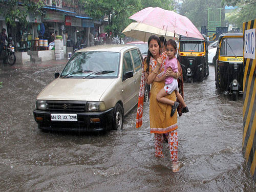 Woman wades through a water logged road while carrying during heavy rains in Thane. PTI Photo.