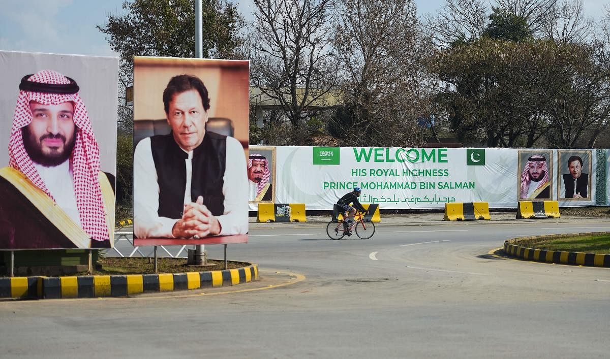 A foreigner rides past billboards showing portraits of Saudi Arabian Crown Prince Mohammed bin Salman (L) and Pakistan's Prime Minister Imran Khan (R) and a banner welcoming the prince ahead of his arrival in Islamabad. AFP