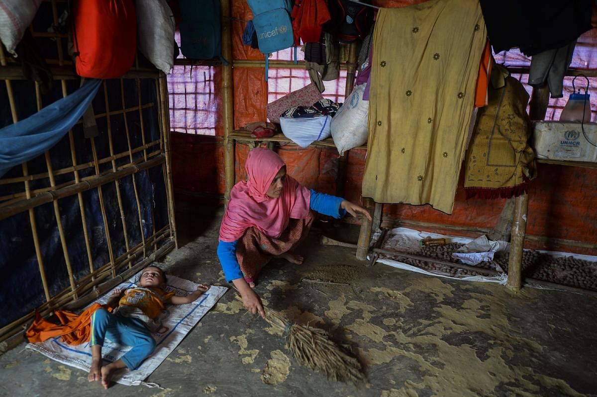 A Rohingya woman cleans her house as her child sleeps next to her at Kutupalong refugee camp in Ukhia on July 24, 2019. (Photo by AFP)