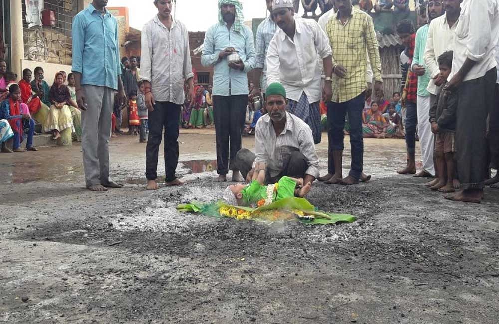 A baby is placed on the embers of Bibi Fatima Panja at Allapura in Kundgol taluk of Dharwad district on Sunday  to fulfil its mother's vow. DH photo.
