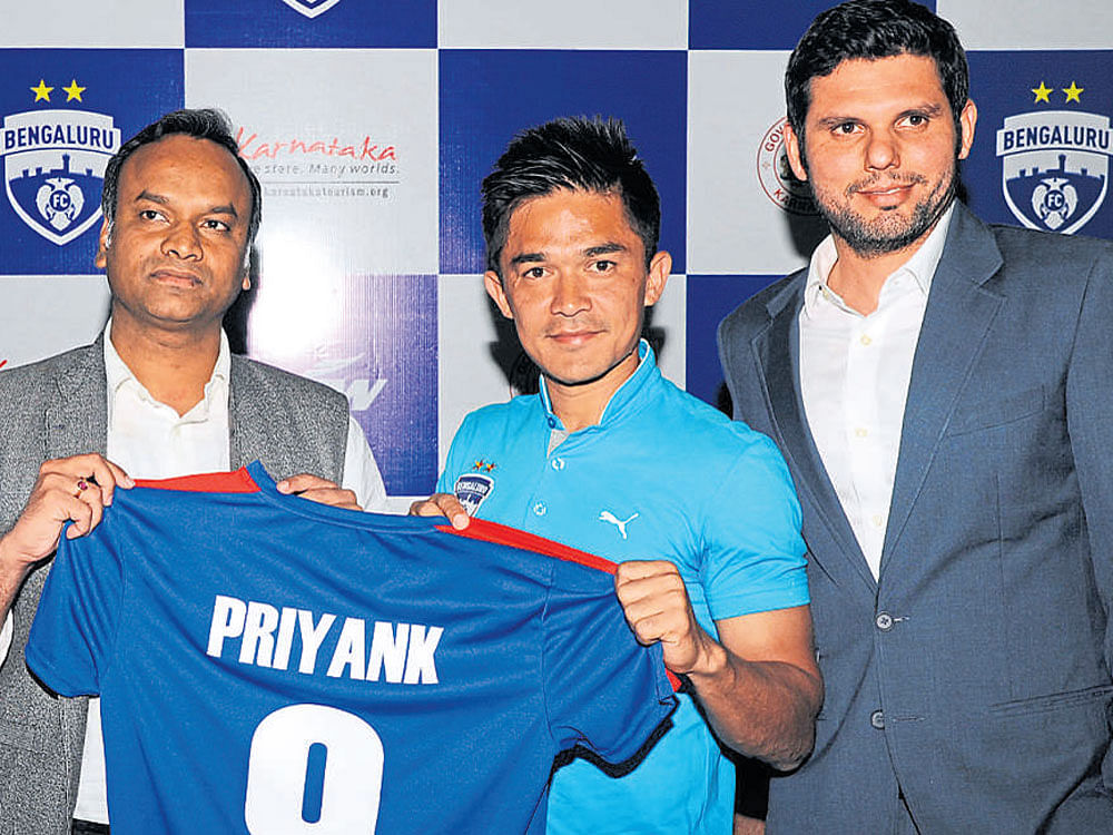 Bengaluru Football Club captain Sunil Chhetri hands over a team jersey to Priyank Kharge, Minister for IT, BT and Tourism, at a press conference to announce the tie-up between the Tourism department and the team in Bengaluru  on Thursday. Team CEO Mustafa Ghouse looks on.
