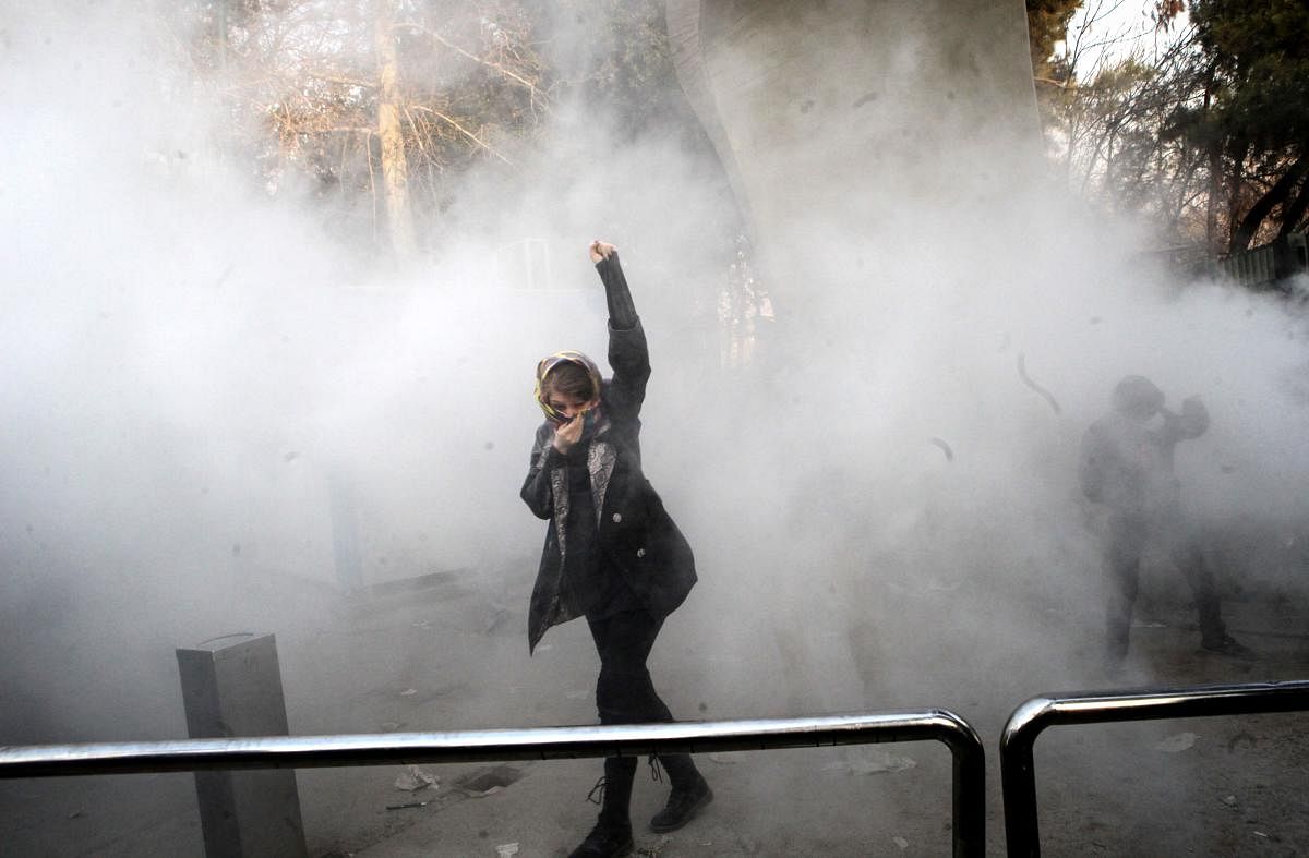 TOPSHOT - An Iranian woman raises her fist amid the smoke of tear gas at the University of Tehran during a protest driven by anger over economic problems, in the capital Tehran on December 30, 2017. Students protested in a third day of demonstrations sparked by anger over Iran's economic problems, videos on social media showed, but were outnumbered by counter-demonstrators. / AFP PHOTO / STR