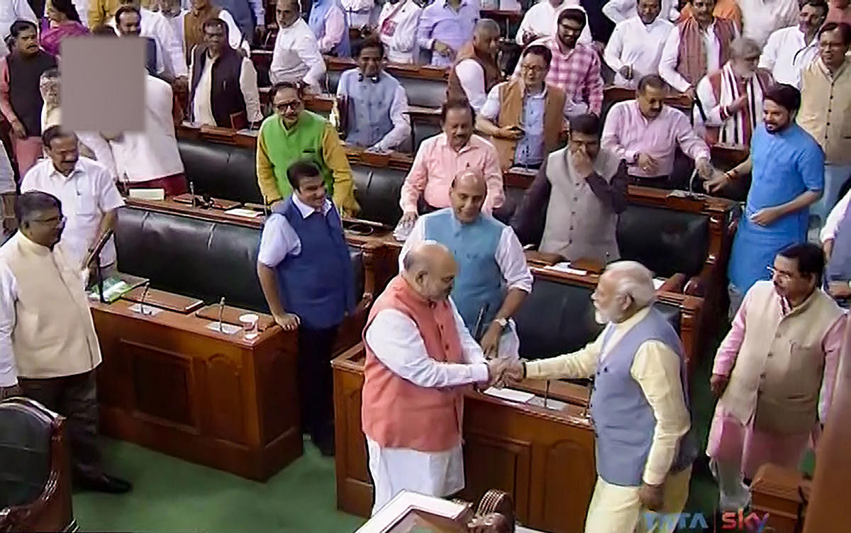 Prime Minister Narendra Modi shakes hands with Union Home Minister Amit Shah after Parliament approved the abrogation of special status given to J&K under Article 370, in the Lok Sabha, in New Delhi. LSTV/PTI